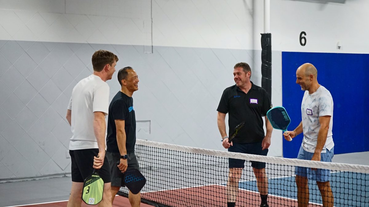 Four players meet at the net after a game, and everyone's laughing at the same moment.